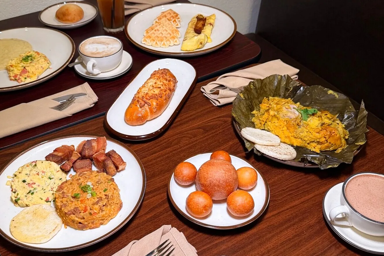 Mesa de desayuno colombiano en Raigal: huevos al gusto, arroz con frijoles, chicharrón, arepa, buñuelos, tamal, pan de queso, café y chocolate caliente